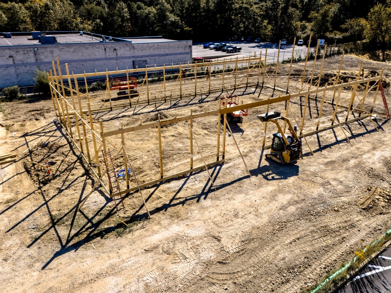 Low aerial view of crews framing the Apex Strength Club walls with a skid steer working alongside the structure